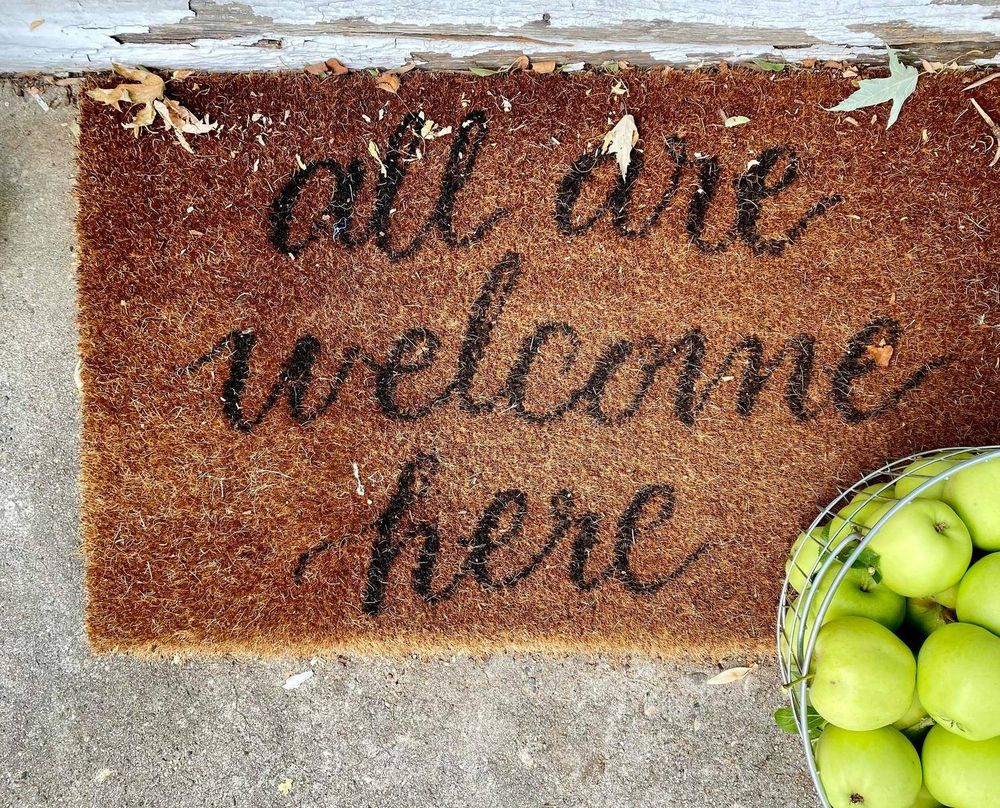 A doormat reading 'all are welcome here' on a front step